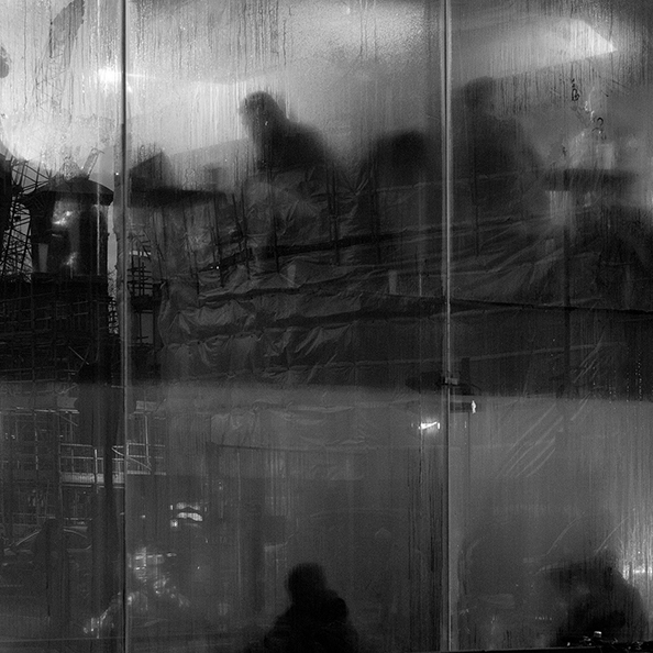 A black and white photo looking into a steamy coffee shop window of people sat at tables working, from the street outside in London.