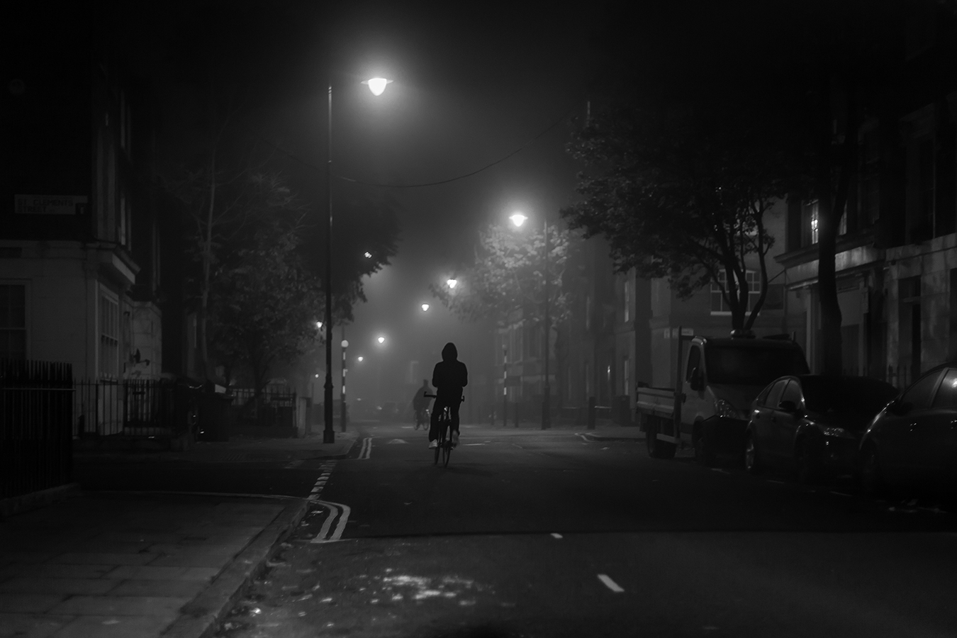 hooded person riding a bike in london at night
