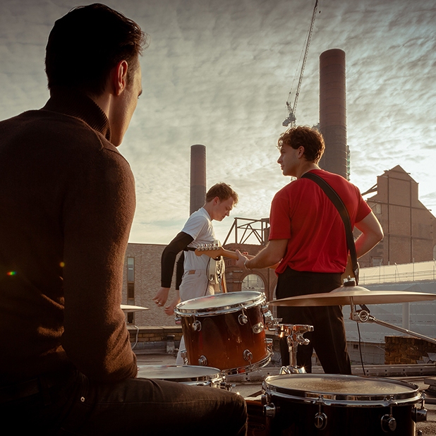 3 male members of a music band on a roof with instruments in London.